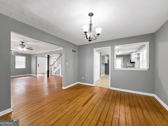 unfurnished room featuring a textured ceiling, plenty of natural light, ceiling fan with notable chandelier, and light hardwood / wood-style flooring