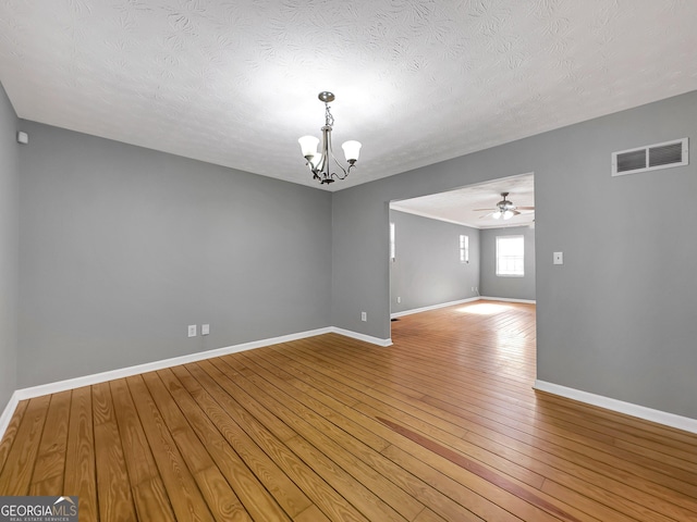 empty room featuring ceiling fan with notable chandelier, a textured ceiling, and hardwood / wood-style floors