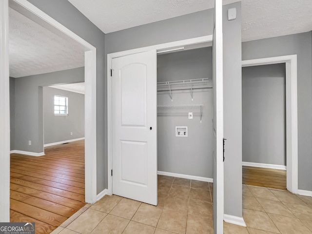 clothes washing area featuring a textured ceiling, hookup for a washing machine, and light tile patterned flooring