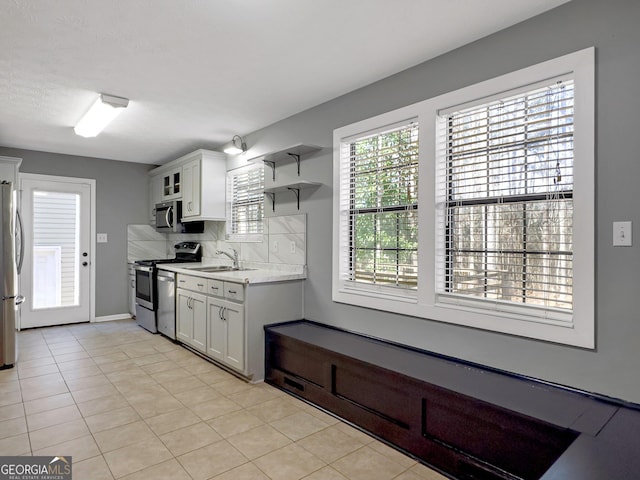 kitchen with light tile patterned floors, white cabinetry, appliances with stainless steel finishes, tasteful backsplash, and sink