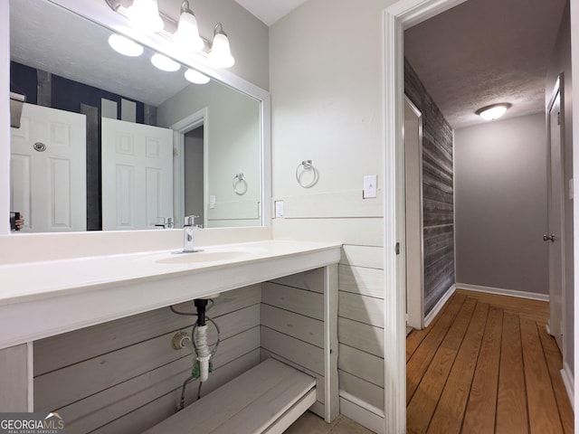 bathroom featuring sink, wood walls, a textured ceiling, and hardwood / wood-style floors