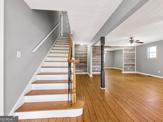 staircase featuring a textured ceiling, ceiling fan, hardwood / wood-style flooring, and wooden walls