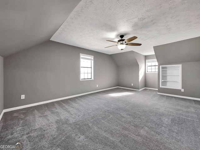 additional living space featuring dark carpet, a textured ceiling, lofted ceiling, ceiling fan, and built in features