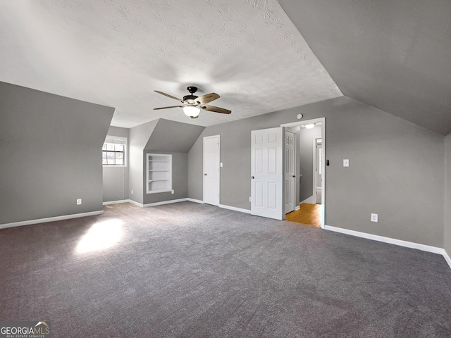 additional living space featuring ceiling fan, a textured ceiling, built in shelves, and vaulted ceiling