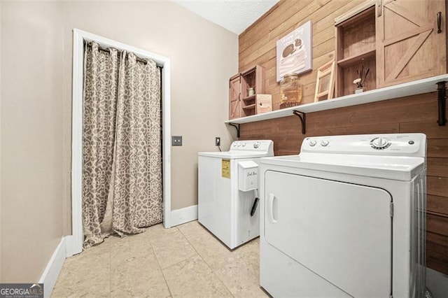 clothes washing area with washing machine and dryer, a textured ceiling, and wooden walls