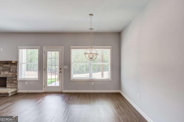 doorway to outside with a notable chandelier, dark hardwood / wood-style flooring, a stone fireplace, and a healthy amount of sunlight