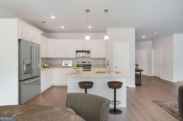 kitchen with appliances with stainless steel finishes, white cabinetry, sink, hanging light fixtures, and light hardwood / wood-style flooring