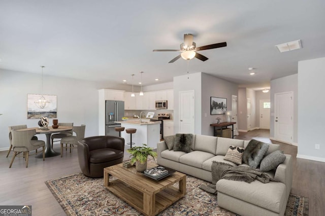 living room with sink, ceiling fan with notable chandelier, and light hardwood / wood-style floors