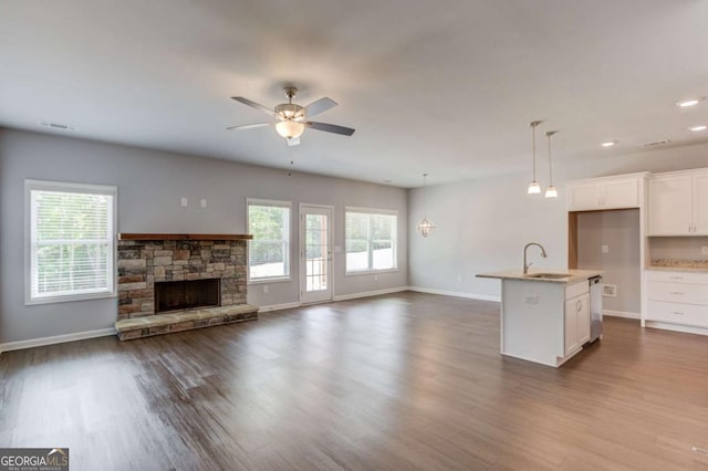 kitchen featuring white cabinets, a stone fireplace, hanging light fixtures, a kitchen island with sink, and ceiling fan