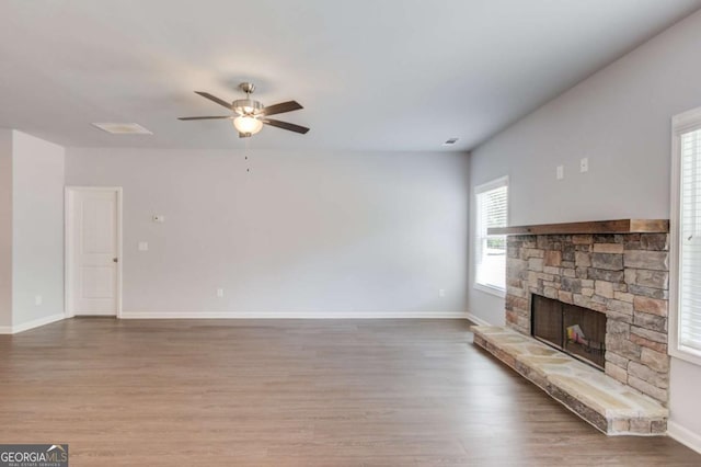 unfurnished living room with ceiling fan, wood-type flooring, and a stone fireplace