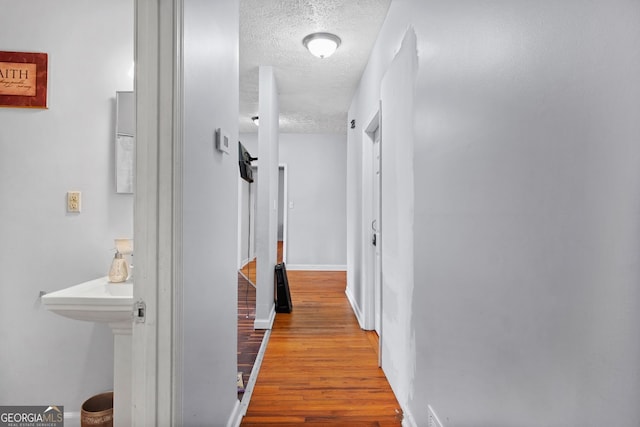 corridor featuring a textured ceiling and light hardwood / wood-style floors