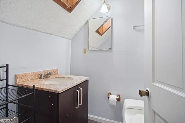 bathroom with toilet, vanity, a textured ceiling, and lofted ceiling