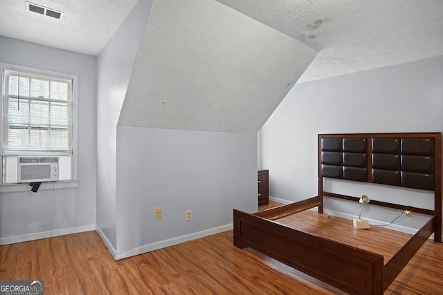 bedroom with lofted ceiling, cooling unit, a textured ceiling, and hardwood / wood-style flooring