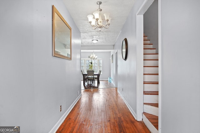 hall with a textured ceiling, a chandelier, and hardwood / wood-style floors