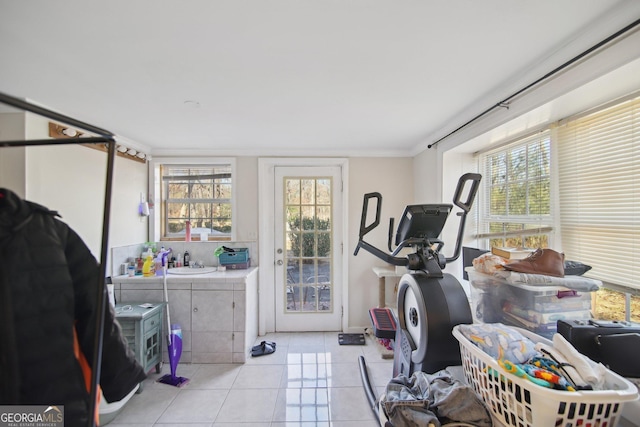 exercise area featuring sink, light tile patterned floors, crown molding, and a healthy amount of sunlight