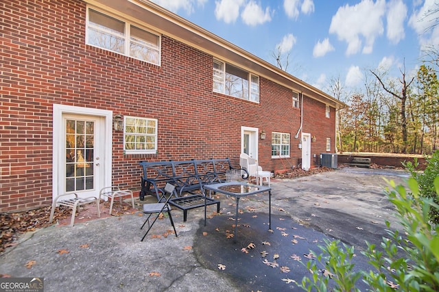 rear view of house with central AC, brick siding, and a patio