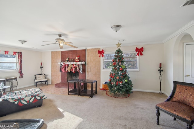 carpeted living room featuring ceiling fan, a brick fireplace, crown molding, and a healthy amount of sunlight