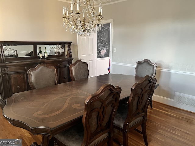 dining space with hardwood / wood-style floors, crown molding, and a chandelier