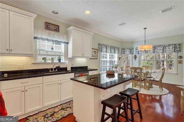 kitchen with decorative light fixtures, a kitchen island, sink, a breakfast bar area, and white cabinets