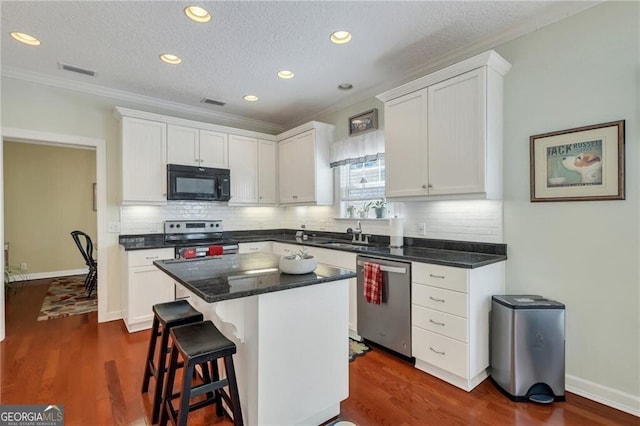 kitchen with white cabinets, appliances with stainless steel finishes, a center island, and dark hardwood / wood-style flooring