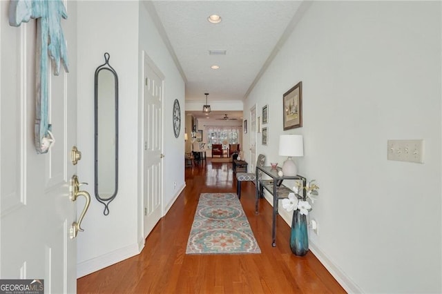 hallway featuring wood-type flooring, crown molding, and a textured ceiling