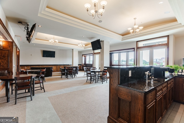 kitchen with light carpet, a raised ceiling, decorative light fixtures, dark stone counters, and a chandelier