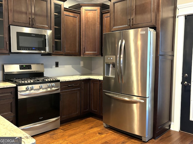 kitchen with stainless steel appliances, light stone countertops, and dark wood-type flooring