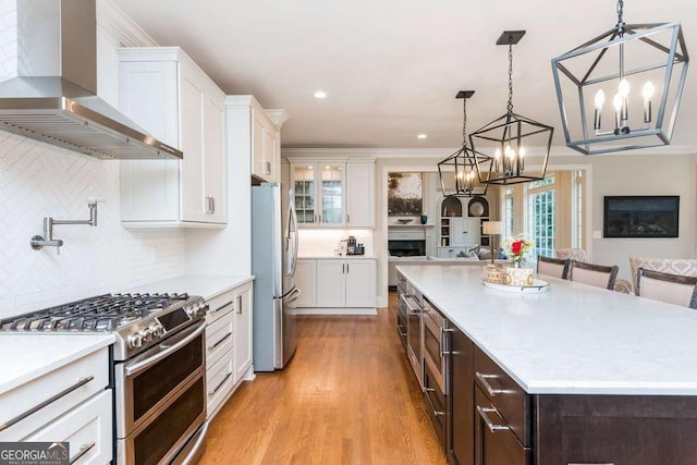 kitchen featuring white cabinets, appliances with stainless steel finishes, wall chimney exhaust hood, decorative light fixtures, and a kitchen breakfast bar