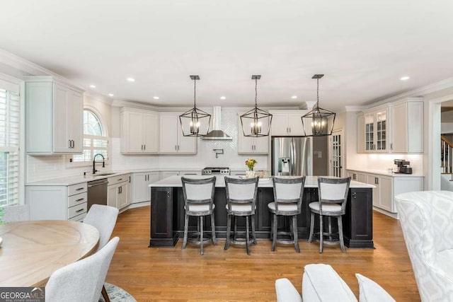 kitchen with decorative light fixtures, a kitchen island, sink, appliances with stainless steel finishes, and wall chimney exhaust hood