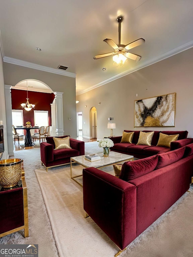 carpeted living room featuring ornate columns, crown molding, and ceiling fan with notable chandelier