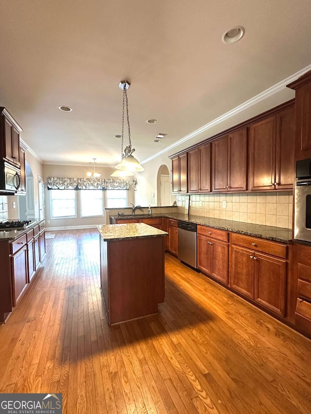 kitchen featuring appliances with stainless steel finishes, a center island, backsplash, hanging light fixtures, and light wood-type flooring