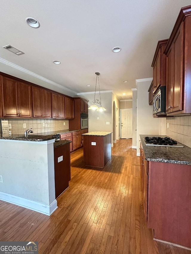 kitchen featuring decorative light fixtures, appliances with stainless steel finishes, ornamental molding, and a kitchen island