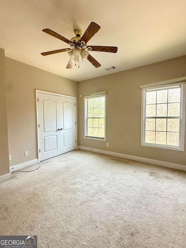 unfurnished bedroom with ceiling fan, multiple windows, and light carpet