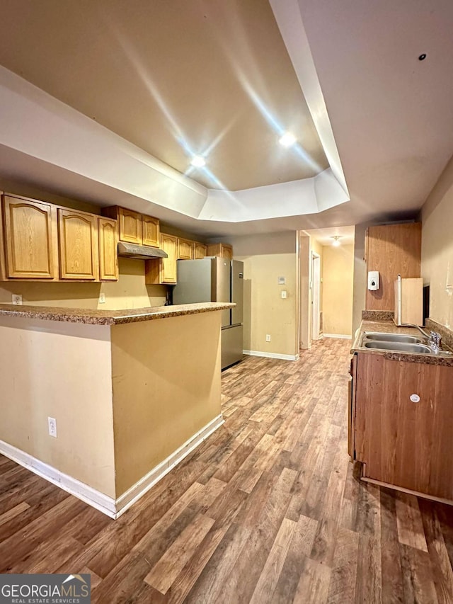 kitchen featuring a raised ceiling, hardwood / wood-style floors, sink, and stainless steel refrigerator