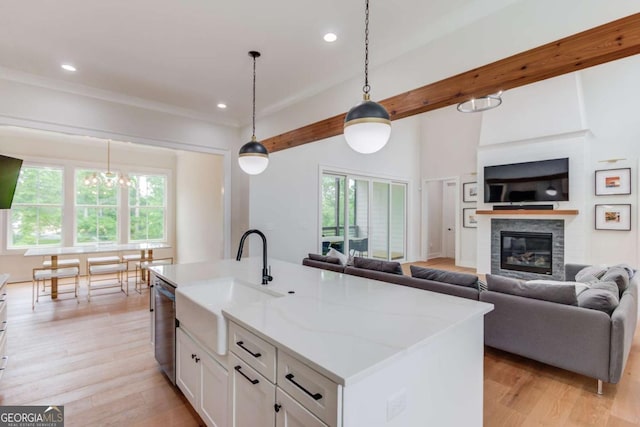 kitchen with dishwasher, a center island with sink, white cabinetry, hanging light fixtures, and light stone countertops