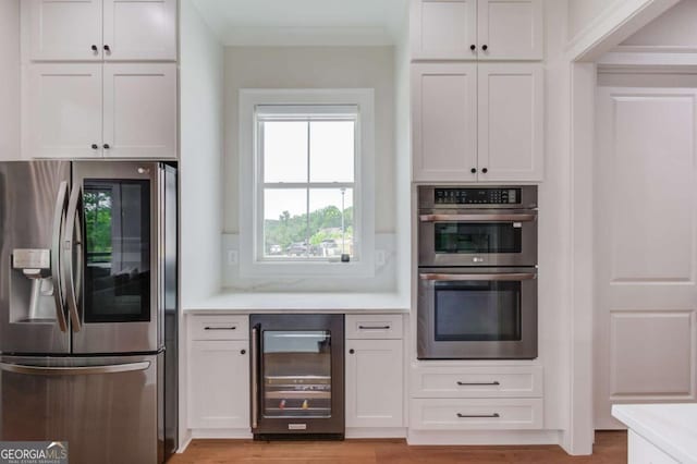 kitchen featuring appliances with stainless steel finishes, crown molding, wine cooler, and white cabinetry