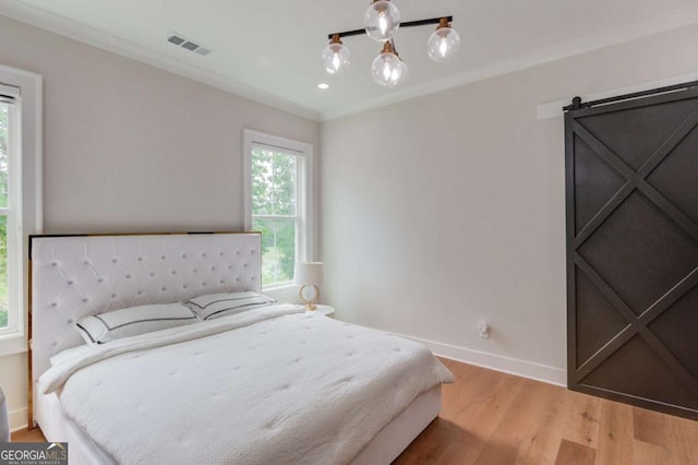 bedroom featuring an inviting chandelier, ornamental molding, a barn door, and light hardwood / wood-style flooring