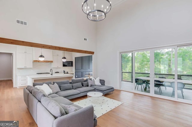 living room with a towering ceiling, a chandelier, and light hardwood / wood-style floors