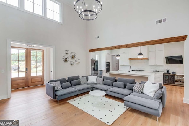 living room with light wood-type flooring, a chandelier, a towering ceiling, and french doors