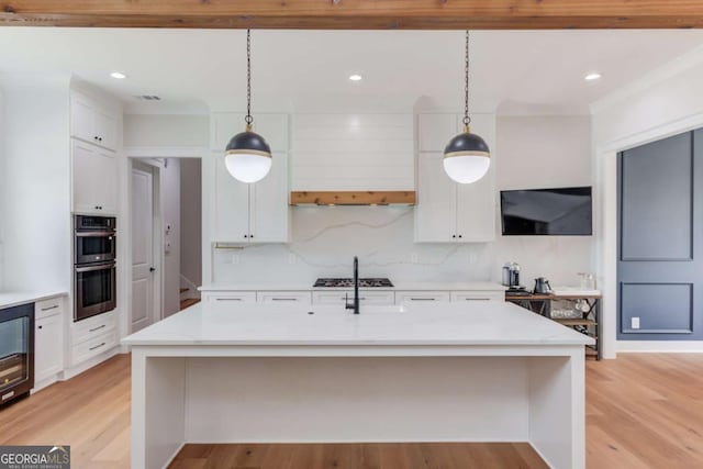 kitchen with stainless steel appliances, light hardwood / wood-style flooring, hanging light fixtures, and an island with sink