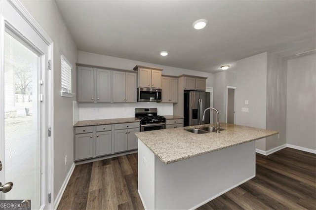 kitchen featuring sink, appliances with stainless steel finishes, gray cabinetry, dark hardwood / wood-style floors, and a center island with sink