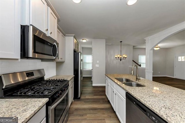 kitchen featuring appliances with stainless steel finishes, white cabinetry, sink, hanging light fixtures, and light stone counters