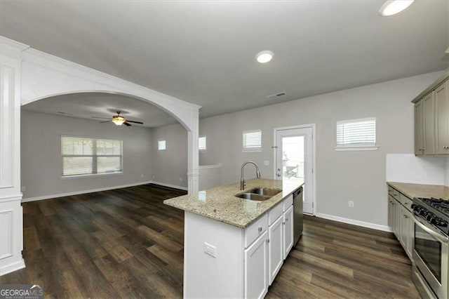 kitchen with dark hardwood / wood-style floors, sink, stainless steel appliances, light stone countertops, and a center island with sink