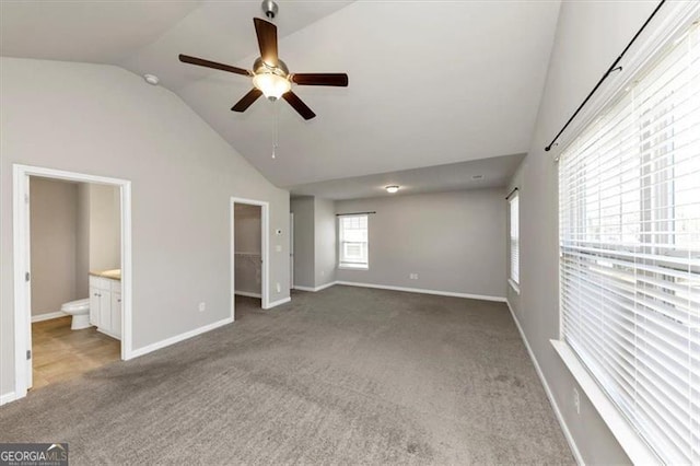 unfurnished bedroom with lofted ceiling, connected bathroom, a walk in closet, light colored carpet, and ceiling fan