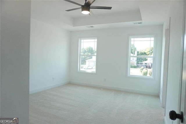 carpeted spare room featuring ceiling fan, plenty of natural light, and a raised ceiling