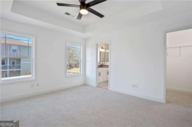 unfurnished bedroom with a spacious closet, ensuite bathroom, ceiling fan, a tray ceiling, and a closet