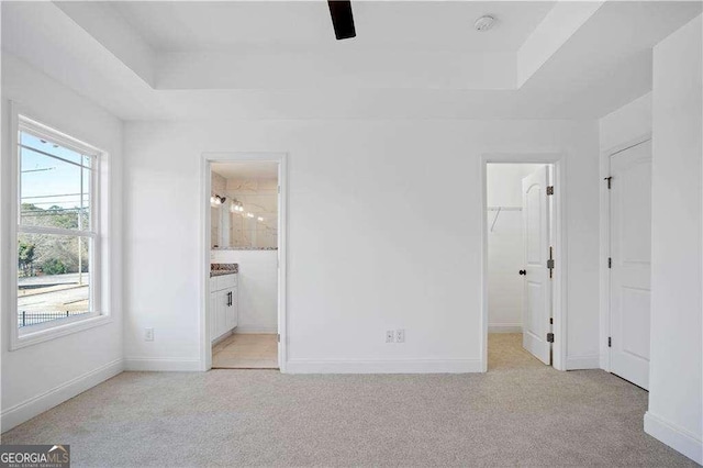 unfurnished bedroom featuring ensuite bathroom, a walk in closet, a closet, and light colored carpet