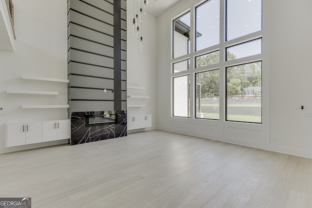 unfurnished living room with light hardwood / wood-style floors and a towering ceiling