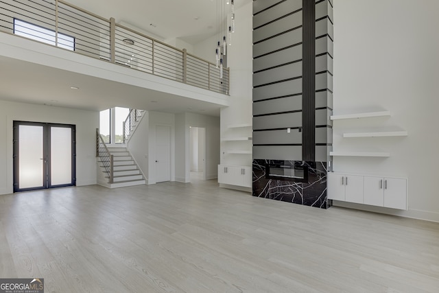 unfurnished living room featuring french doors, a high ceiling, and light hardwood / wood-style floors