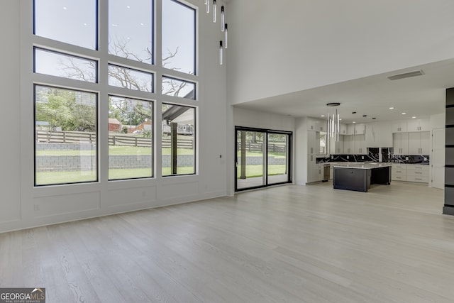 unfurnished living room featuring a towering ceiling and light wood-type flooring